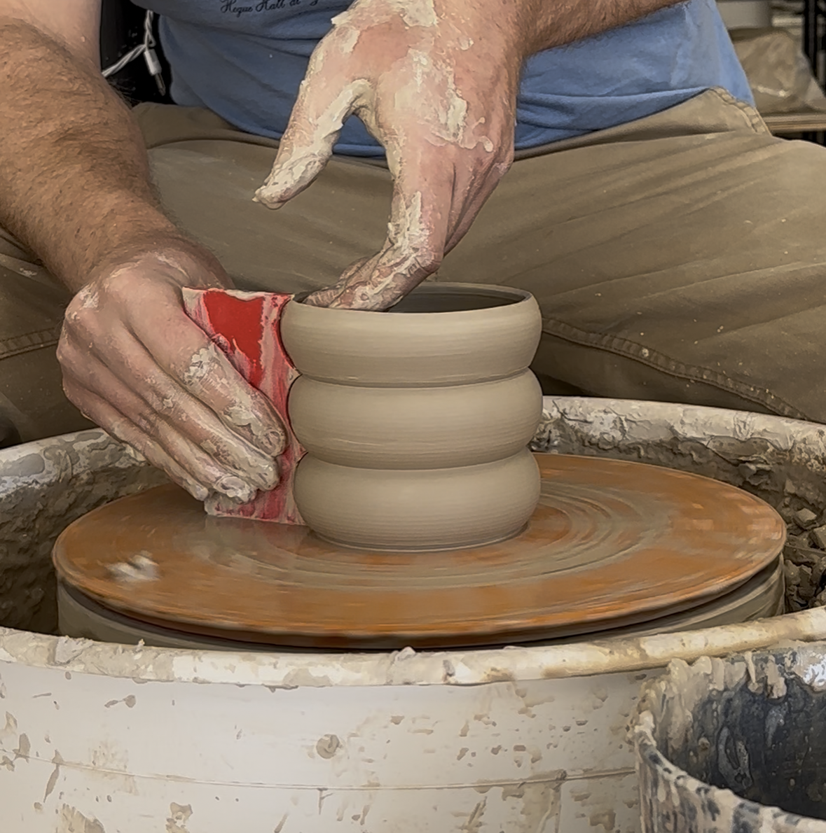 red plastic rib being used to shape a pot on the pottery wheel