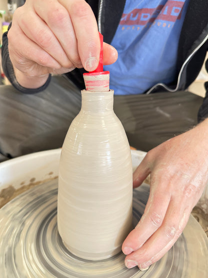 red plastic oi stopper being used to set the size of a bottle on the pottery wheel